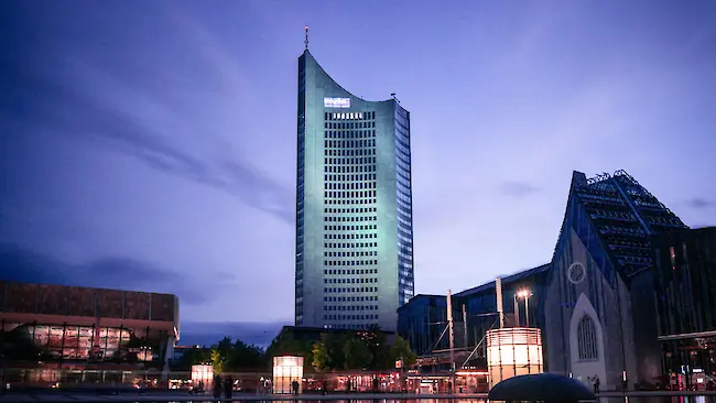 Blaue Abendstimmung am zentralen Teich in Leipzig, im Hintergrund spiegeln sich ein beleuchtetes Hochhaus und das Universitätsgebäude im Wasser.