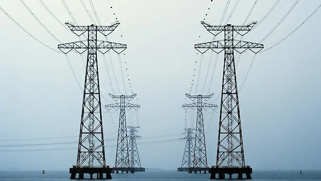 Ein Hochspannungsturm vor einem bewölkten Himmel, mit Stromleitungen, die sich diagonal durch das Bild ziehen und industrielle Dimension sowie elektrische Infrastruktur betonen