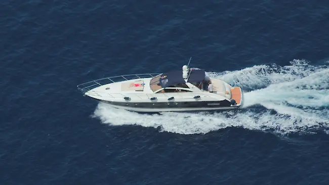 Eine elegante weiße Motorjacht fährt aus der Vogelperspektive über tiefblaues Meer und hinterlässt eine schaumige Spur.